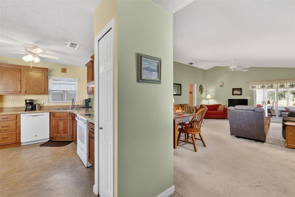 A kitchen with wood cabinets and a dishwasher opens into a carpeted living and dining area — 4900 HERON RUN CIRCLE, LEESBURG, FL