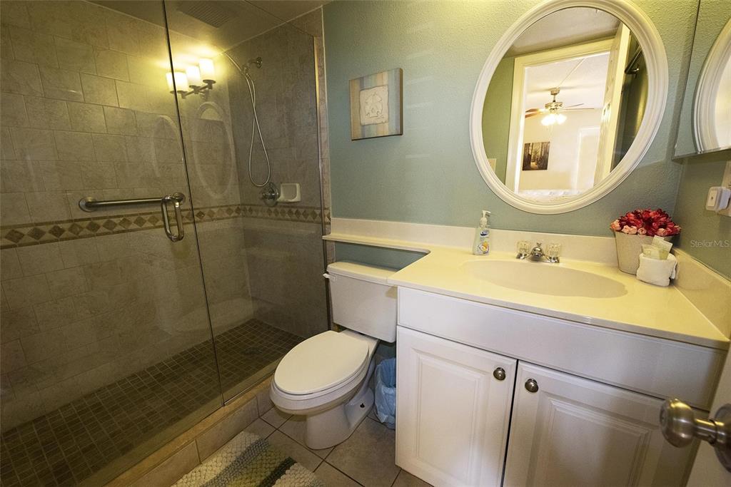 A bathroom features a glass-enclosed shower, a white vanity with a sink, and a toilet — 1571 S ATLANTIC AVENUE UNIT 105, NEW SMYRNA BEACH, FL