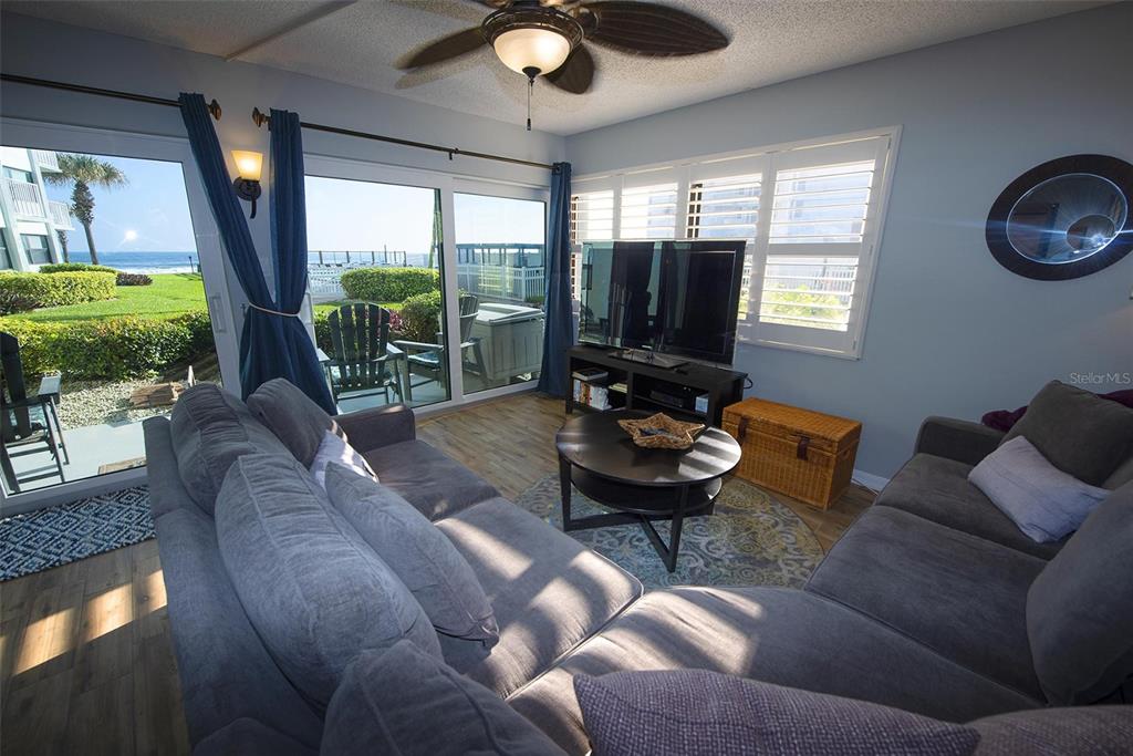 A living room features gray sofas, a round coffee table, and sliding doors overlooking the ocean — 1571 S ATLANTIC AVENUE UNIT 105, NEW SMYRNA BEACH, FL