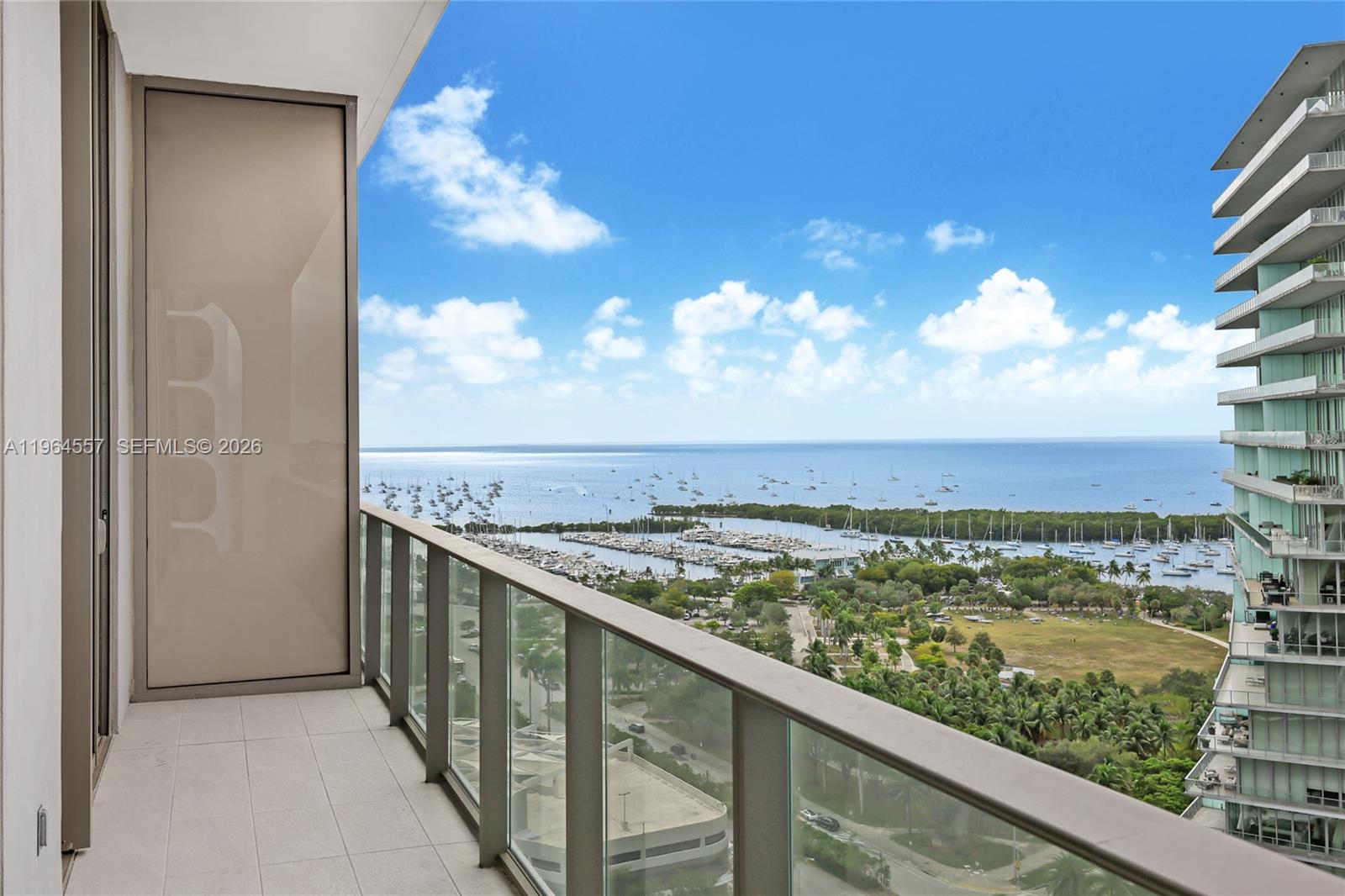 A high-rise balcony with a glass railing overlooks a marina, park, and the ocean — 2655 S Bayshore Dr # 1709, Miami FL 33133, MIAMI, FL