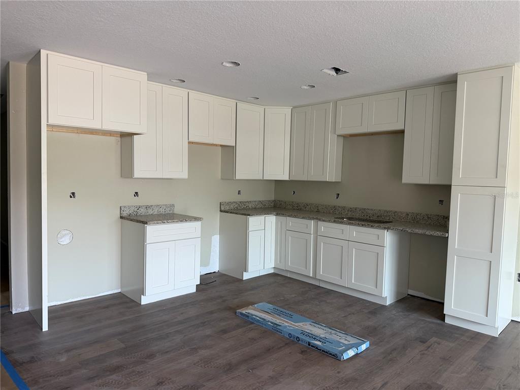 An unfinished kitchen features white shaker cabinets, granite countertops, and wood-look flooring — 13797 SE 40TH COURT, SUMMERFIELD, FL