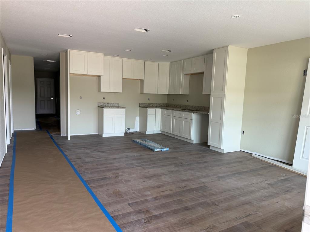 An unfinished kitchen features white cabinets, granite countertops, and wood-look flooring in an open space — 13797 SE 40TH COURT, SUMMERFIELD, FL