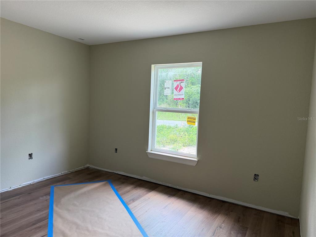 An empty bedroom features light-colored walls, wood-look flooring, and a single window with construction stickers — 13797 SE 40TH COURT, SUMMERFIELD, FL