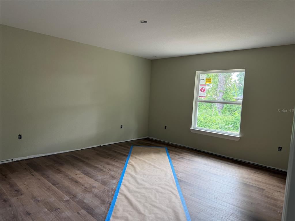 An empty room features light green walls, wood-look flooring, and a single window — 13797 SE 40TH COURT, SUMMERFIELD, FL