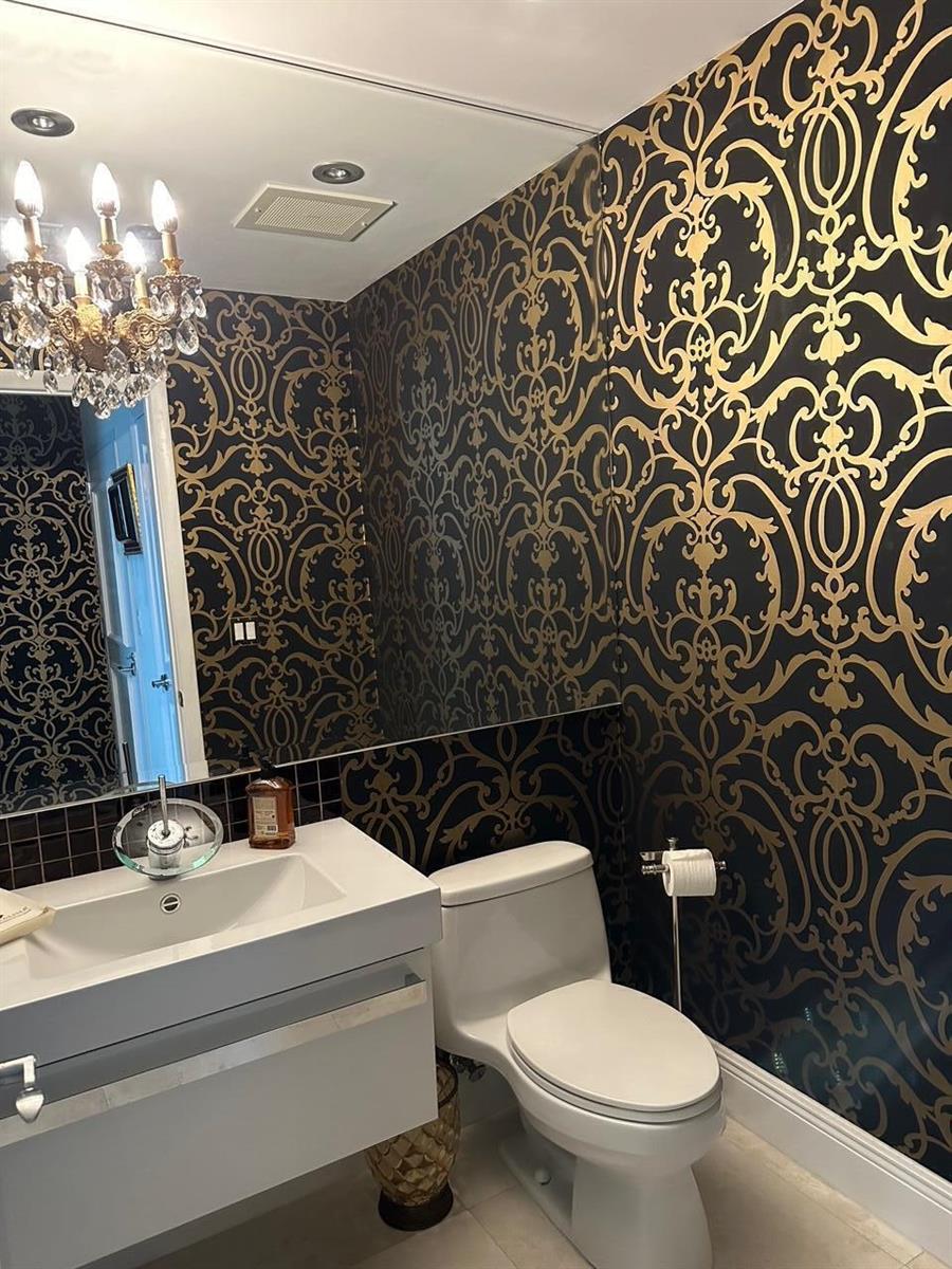 A bathroom features black and gold damask wallpaper, a modern white vanity, and a crystal chandelier — 1945 S Ocean Drive # 609, Hallandale Beach FL 33009, HALLANDALE BEACH, FL