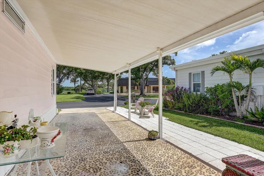 A covered carport with a pebble-textured floor leads to a paved walkway and lawn area — 174 CLUBVIEW DRIVE UNIT 4, SAFETY HARBOR, FL