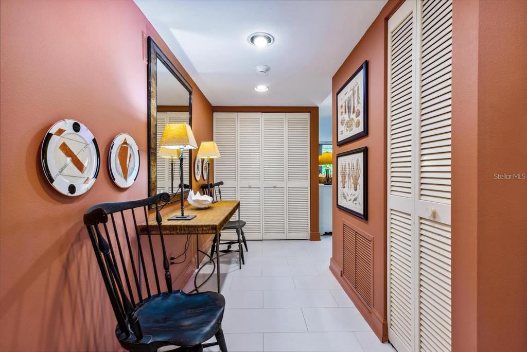 A hallway with terracotta walls, white tiled floors, louvered closet doors, and a wooden console table — 840 BAYPORT WAY UNIT 840, LONGBOAT KEY, FL