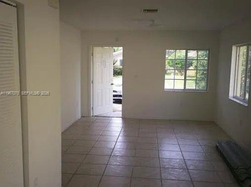 An empty room with light-colored tile flooring, white walls, a window, and an open door — 937 SW 8th Pl, Florida City FL 33034, FLORIDA CITY, FL