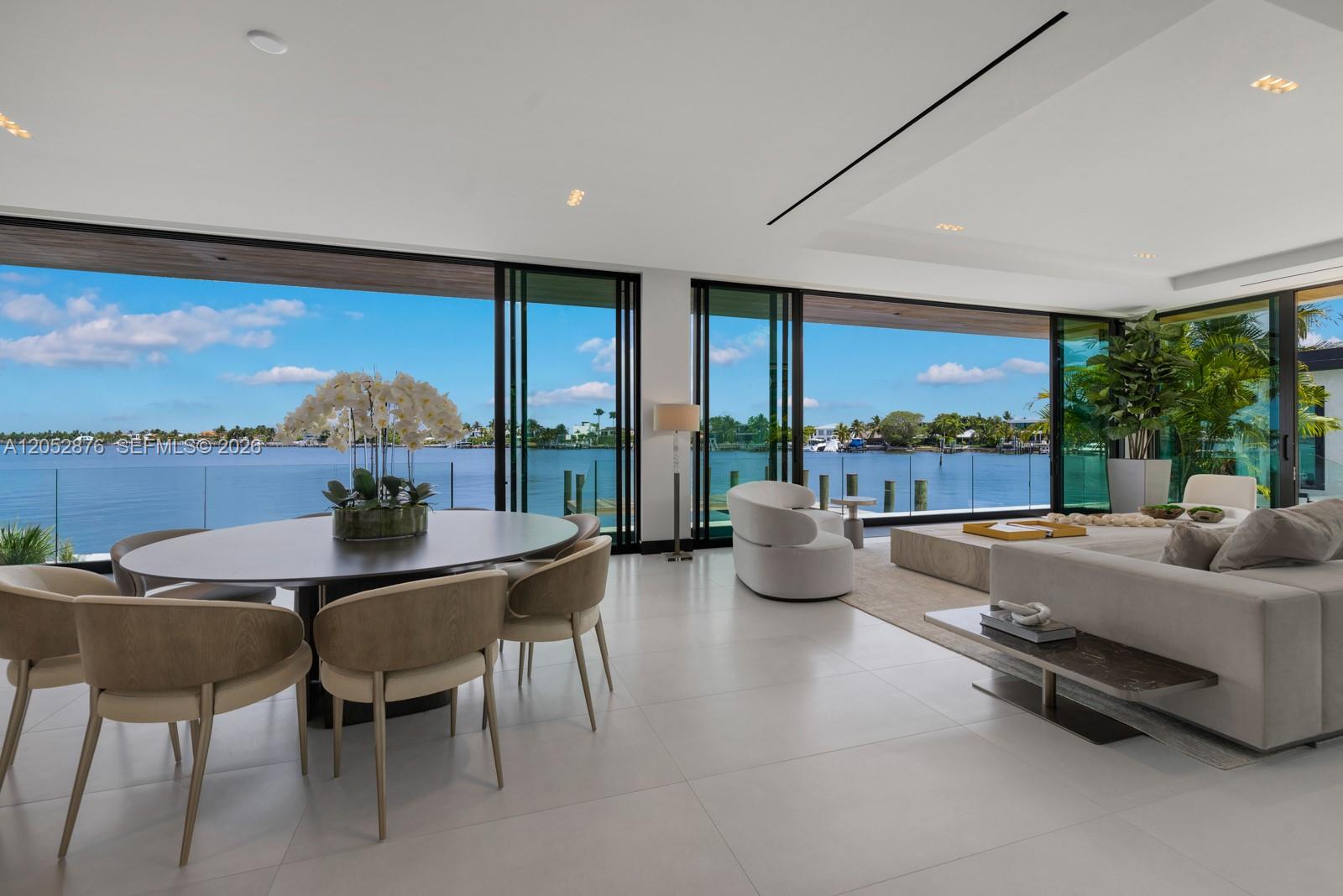 A modern open-plan living and dining area features floor-to-ceiling glass walls overlooking a waterfront — 1141 N Biscayne Point Rd, Miami Beach FL 33141, MIAMI BEACH, FL