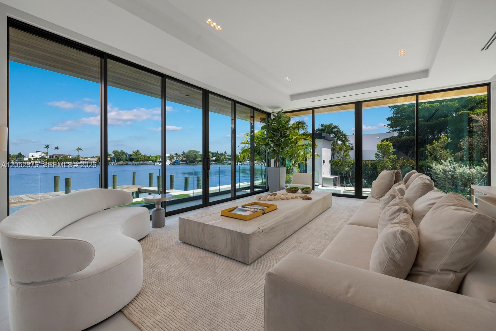 A modern living room features floor-to-ceiling windows overlooking a waterfront canal with a private dock — 1141 N Biscayne Point Rd, Miami Beach FL 33141, MIAMI BEACH, FL