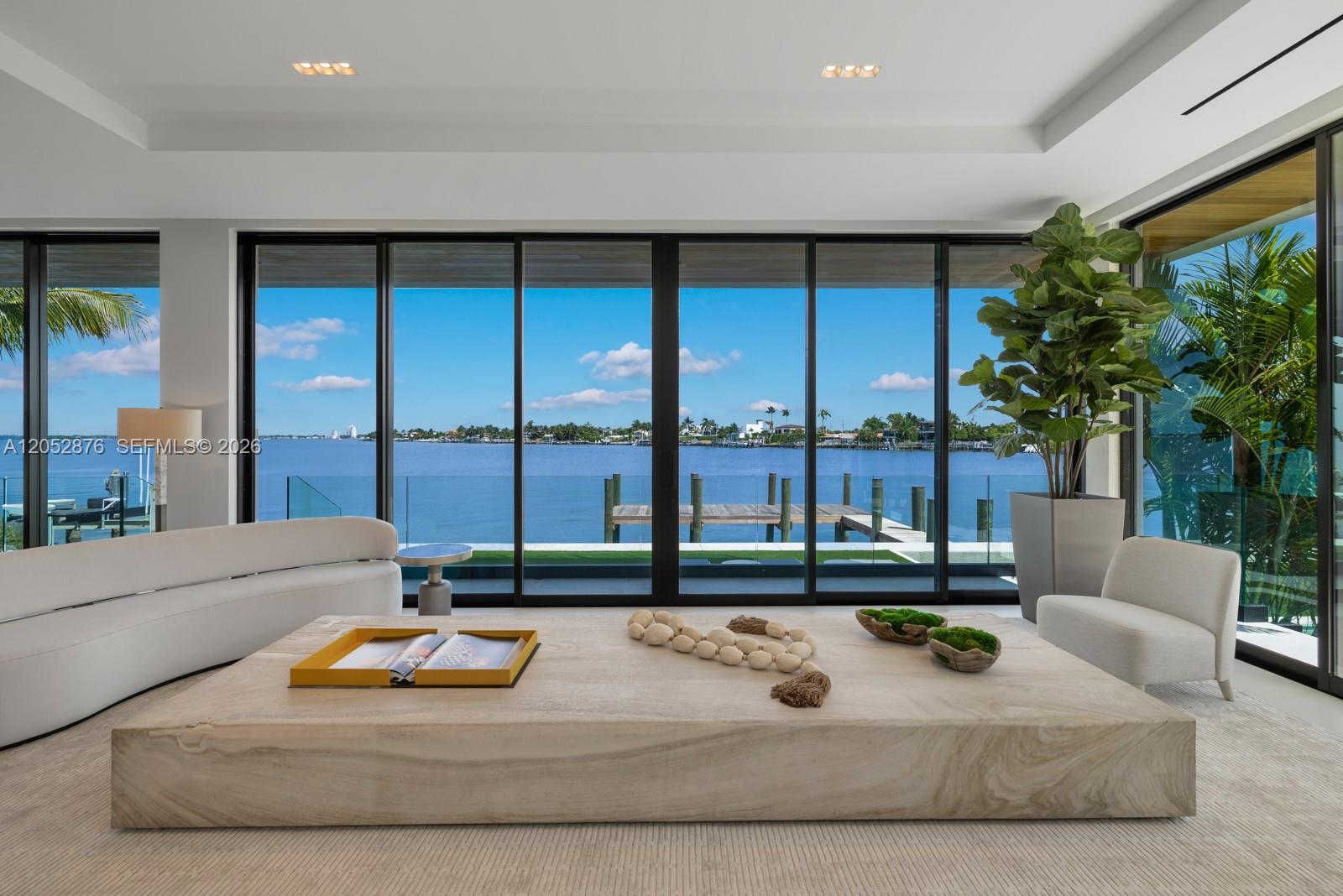 A modern living room features a large stone coffee table overlooking a waterfront dock view — 1141 N Biscayne Point Rd, Miami Beach FL 33141, MIAMI BEACH, FL