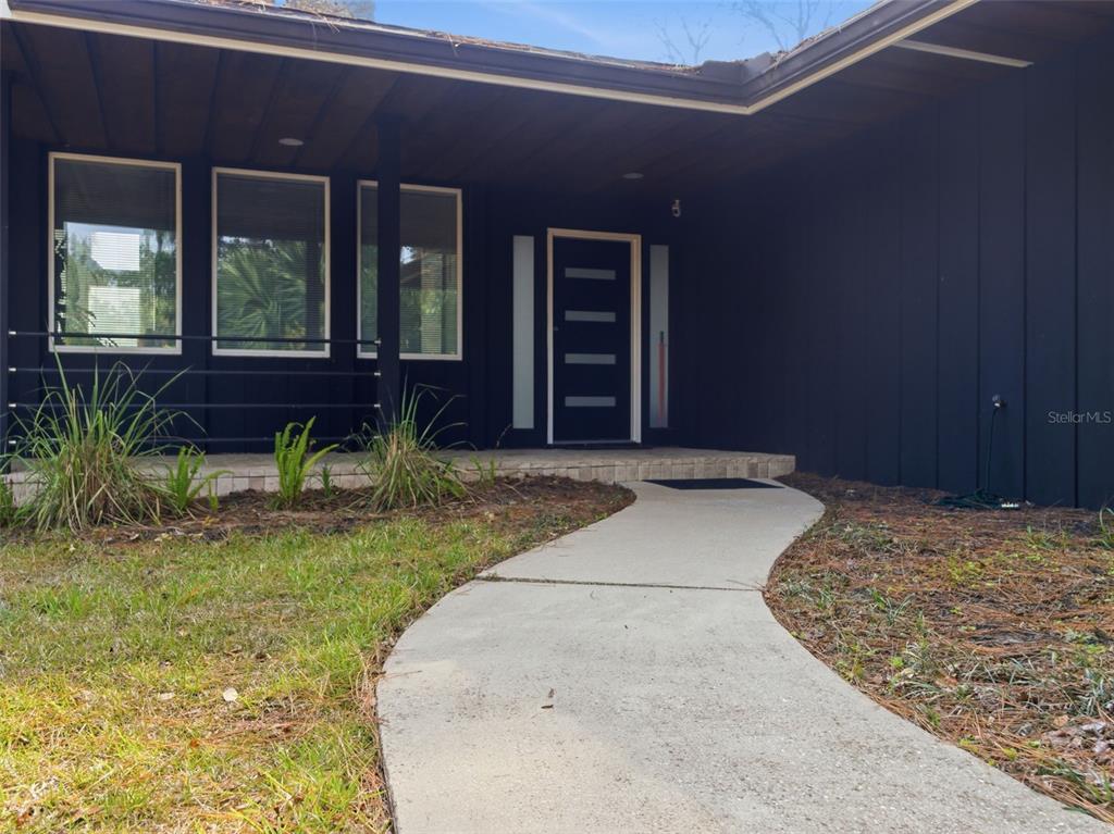 A curved concrete walkway leads to the dark-painted exterior and modern front door of a house — 6201 SW 37TH WAY, GAINESVILLE, FL