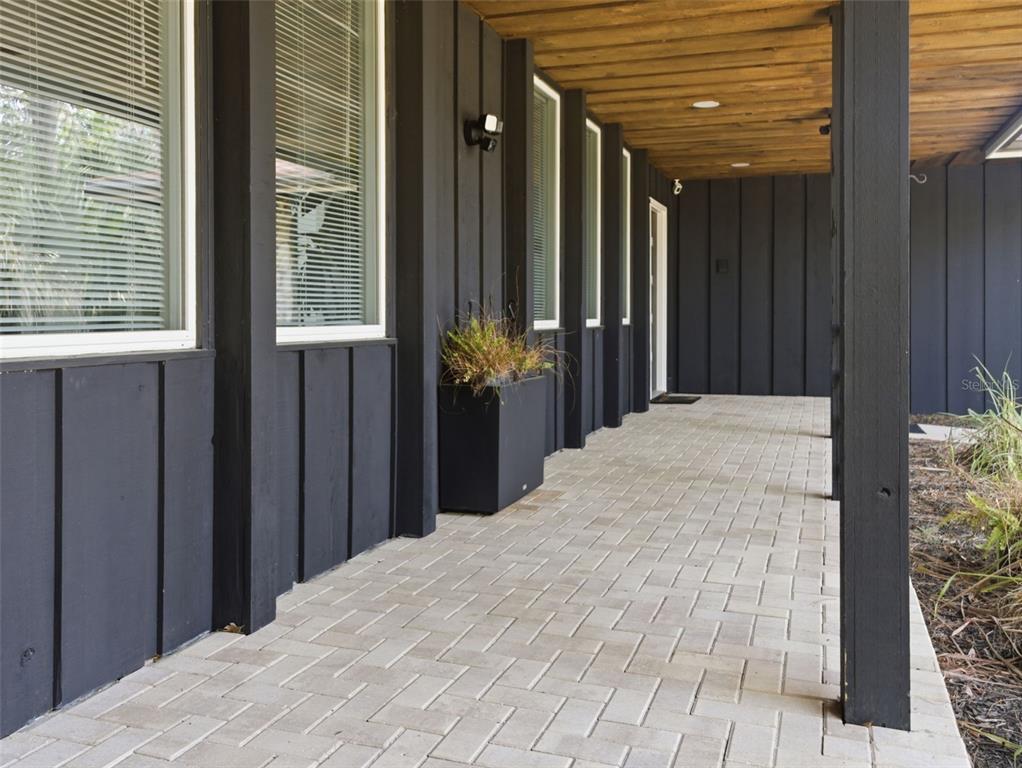 A covered porch features dark vertical siding, light brick pavers, and a wood-paneled ceiling — 6201 SW 37TH WAY, GAINESVILLE, FL