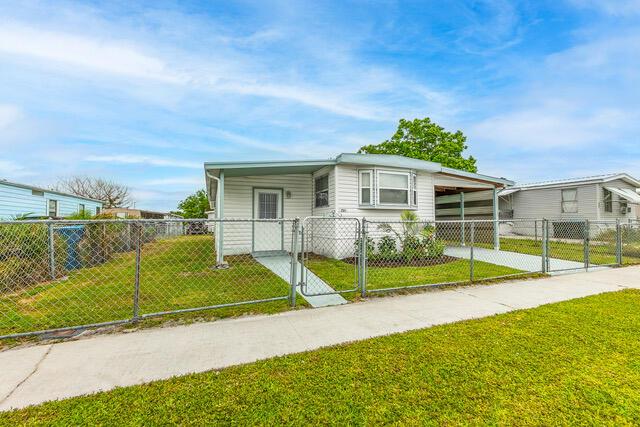 A single-story mobile home with a carport and chain-link fence sits on a grassy lot — 2531 Chatham Way NE, Palm Bay FL 32905, PALM BAY, FL