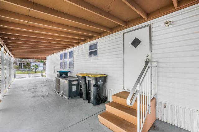 A covered carport area features a white door with stairs, two trash bins, and an AC unit — 2531 Chatham Way NE, Palm Bay FL 32905, PALM BAY, FL