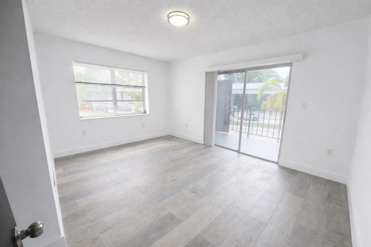 An empty bedroom with white walls, light wood-look flooring, a window, and a sliding glass door — 3300 S Dixie Highway # 503, Miami FL 33133, MIAMI, FL