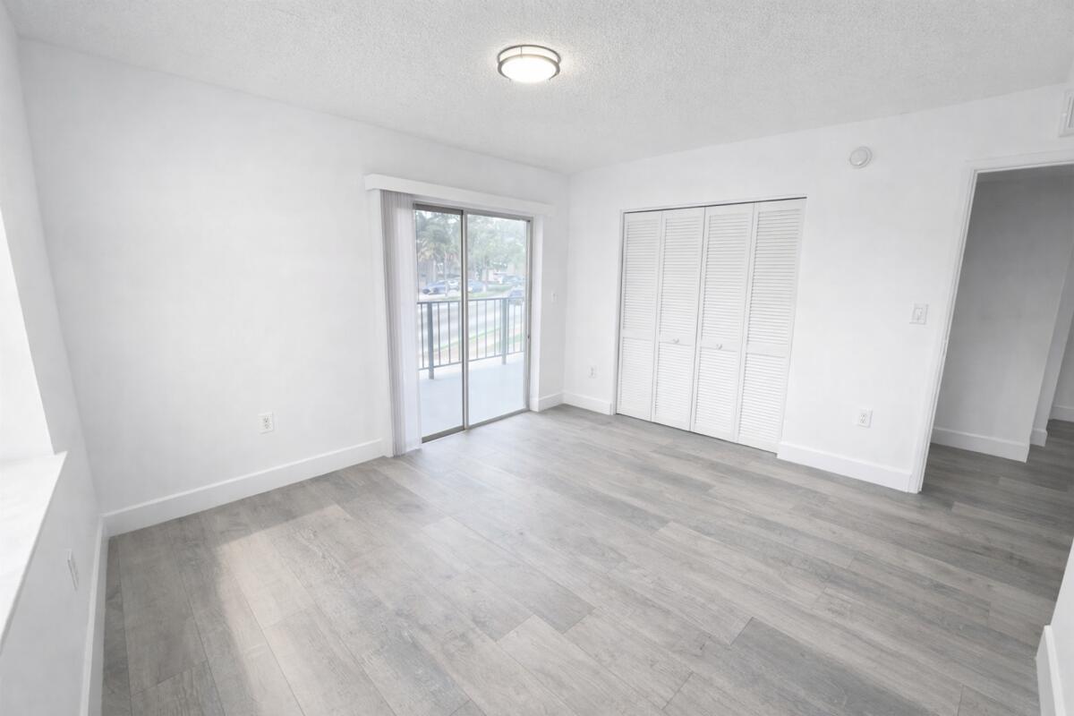 An empty room with light wood-look flooring, white walls, sliding glass doors, and closet doors — 3300 S Dixie Highway # 503, Miami FL 33133, MIAMI, FL