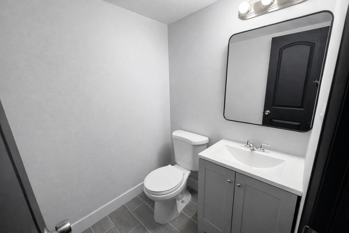 A small bathroom features a gray vanity, a white toilet, and a black-framed mirror — 3300 S Dixie Highway # 503, Miami FL 33133, MIAMI, FL
