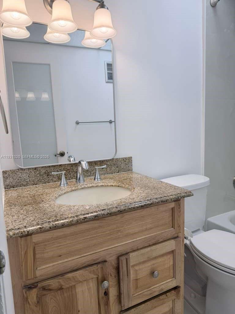 A bathroom features a granite vanity countertop, a wooden cabinet, and a wall-mounted mirror — 160 SW 30th Ave # 104A, Miami FL 33135, MIAMI, FL