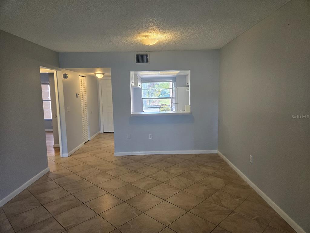 A living area with light blue walls, tile flooring, and a pass-through window to the kitchen — 6328 7TH AVENUE W UNIT 6328, BRADENTON, FL