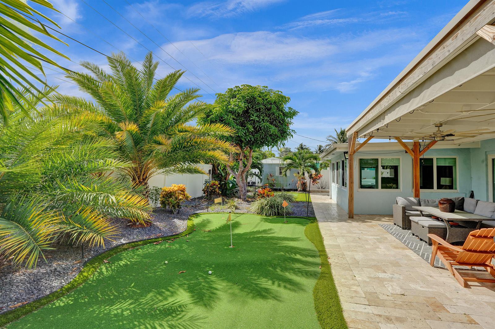 A backyard features a putting green, a covered patio with seating, and various tropical plants — 604 NE 25th Avenue, Pompano Beach FL 33062, POMPANO BEACH, FL