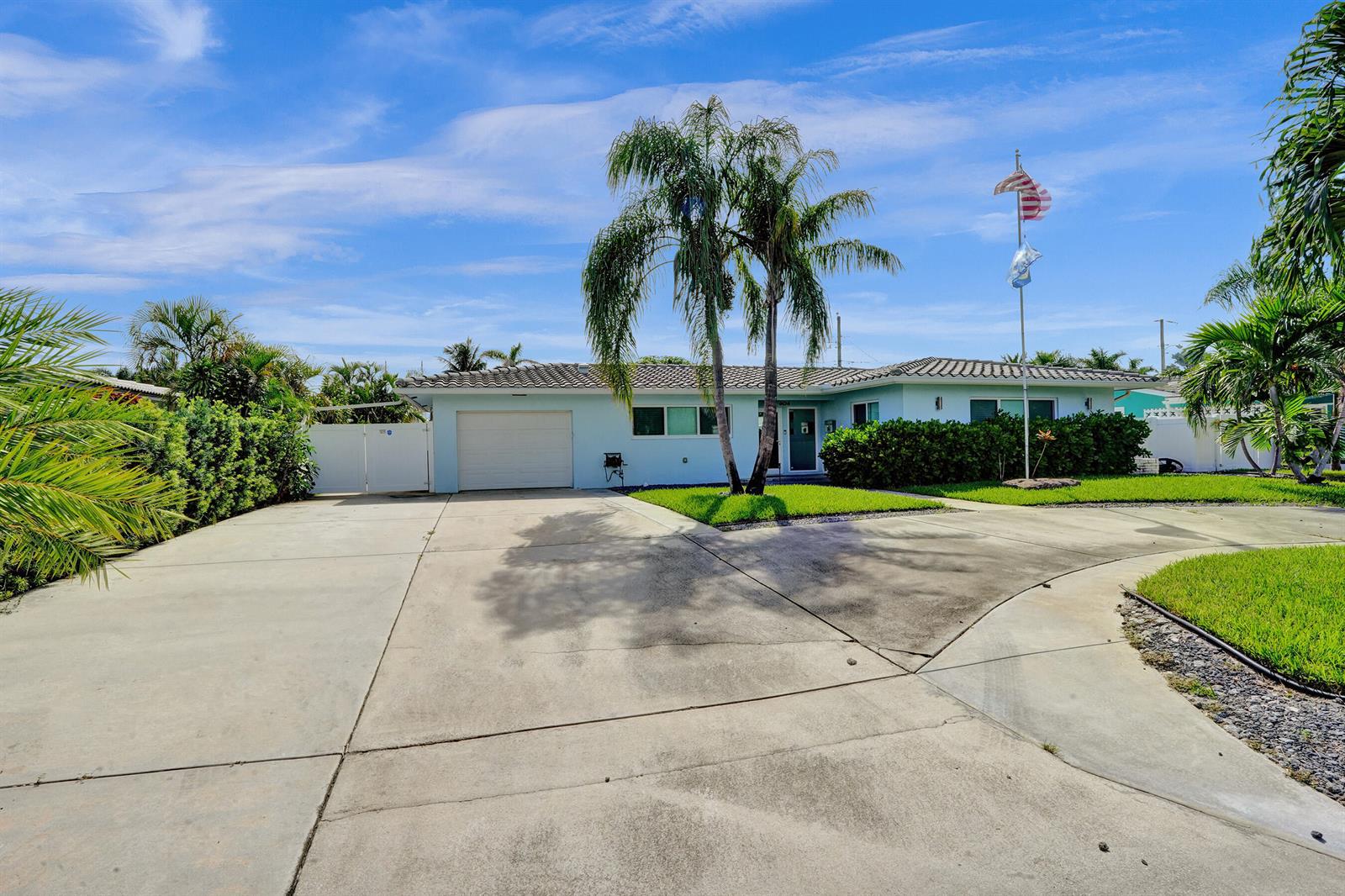 A light blue single-story house features a concrete driveway, a palm tree, and a flagpole — 604 NE 25th Avenue, Pompano Beach FL 33062, POMPANO BEACH, FL