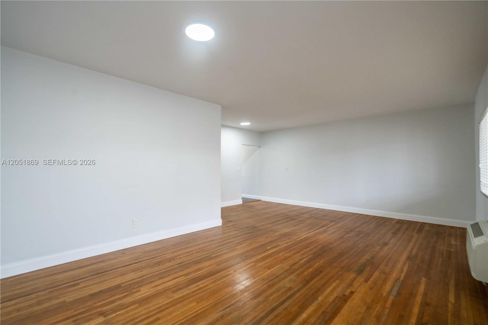 An empty room features light gray walls, hardwood flooring, and a ceiling-mounted light fixture — 8330 Byron Ave # 7, Miami Beach FL 33141, MIAMI BEACH, FL