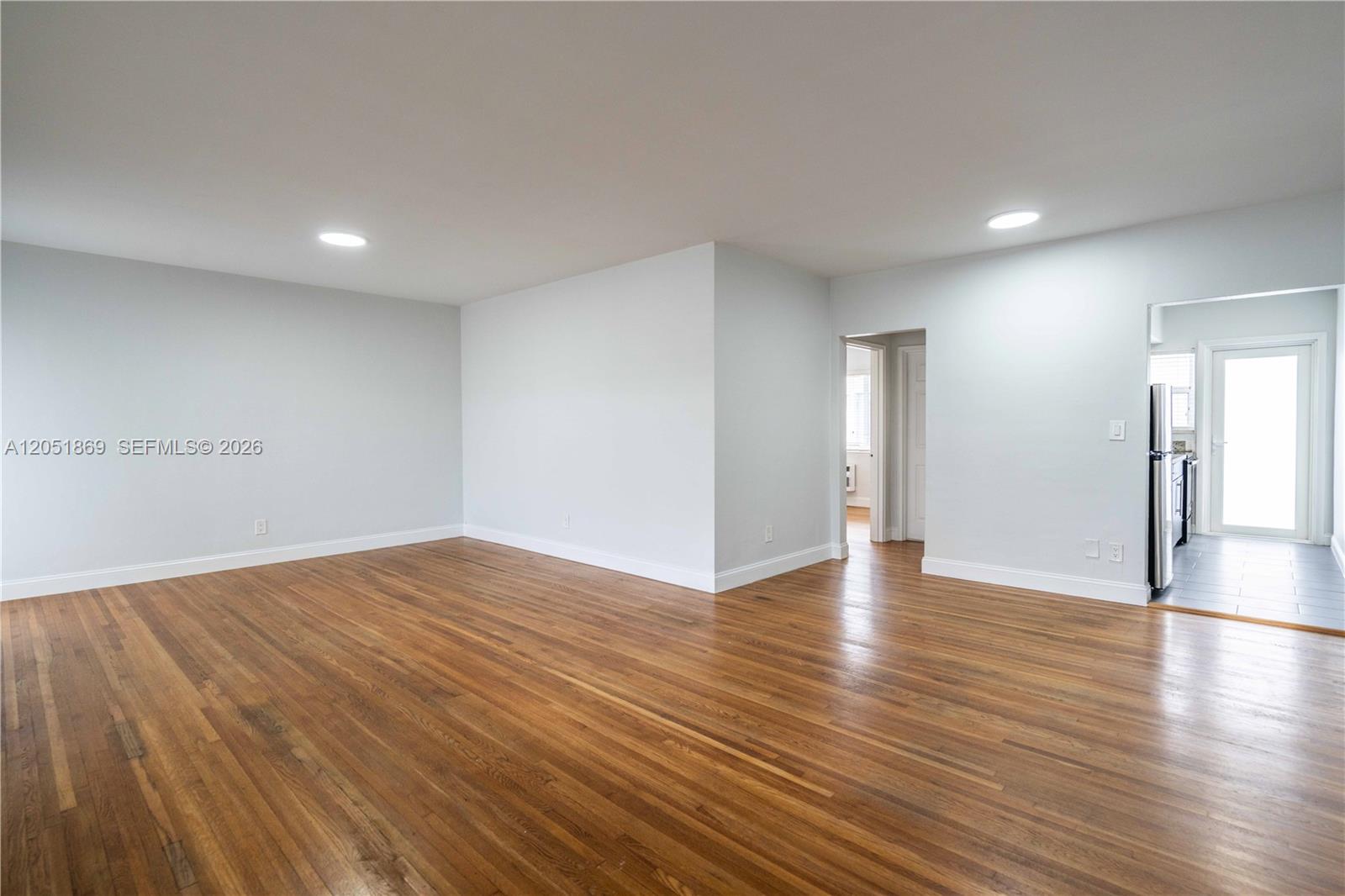 An empty room features light-colored walls, hardwood flooring, and a doorway leading to a kitchen — 8330 Byron Ave # 7, Miami Beach FL 33141, MIAMI BEACH, FL