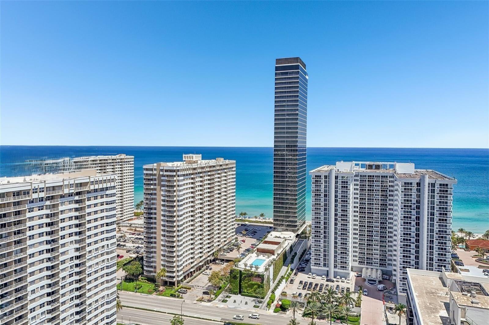 An aerial view shows a tall, dark glass skyscraper surrounded by white residential apartment buildings — 2000 S Ocean Drive SE # 5a, Hallandale Beach FL 33009, HALLANDALE BEACH, FL