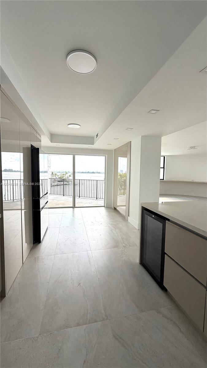 A modern kitchen with light tile flooring leads to a balcony overlooking the water — 1800 NE 114th # 604, North Miami FL 33181, NORTH MIAMI, FL