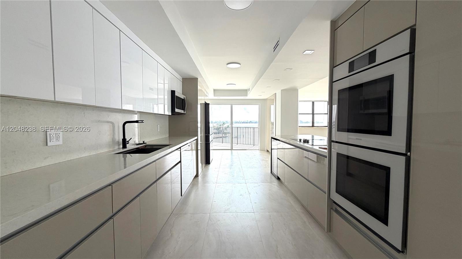 A modern galley kitchen features white cabinetry, stainless steel appliances, and a view of water — 1800 NE 114th # 604, North Miami FL 33181, NORTH MIAMI, FL
