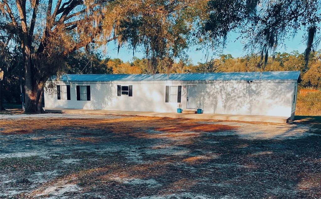 A single-story white mobile home with a metal roof sits on a dirt lot — 8771 NE 107TH COURT, BRONSON, FL