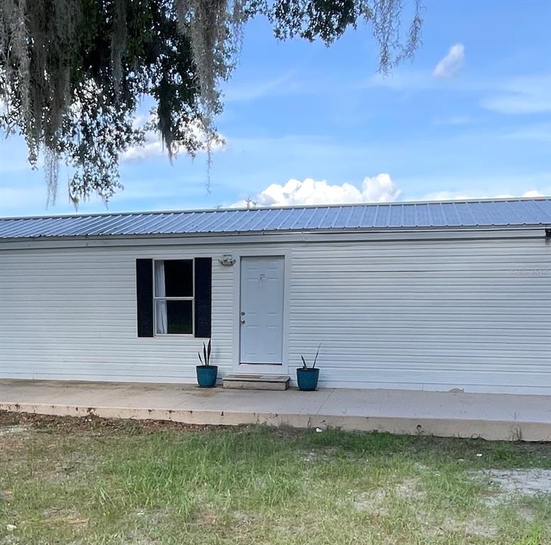 The exterior of a white mobile home features a metal roof, a window, and a door — 8771 NE 107TH COURT, BRONSON, FL