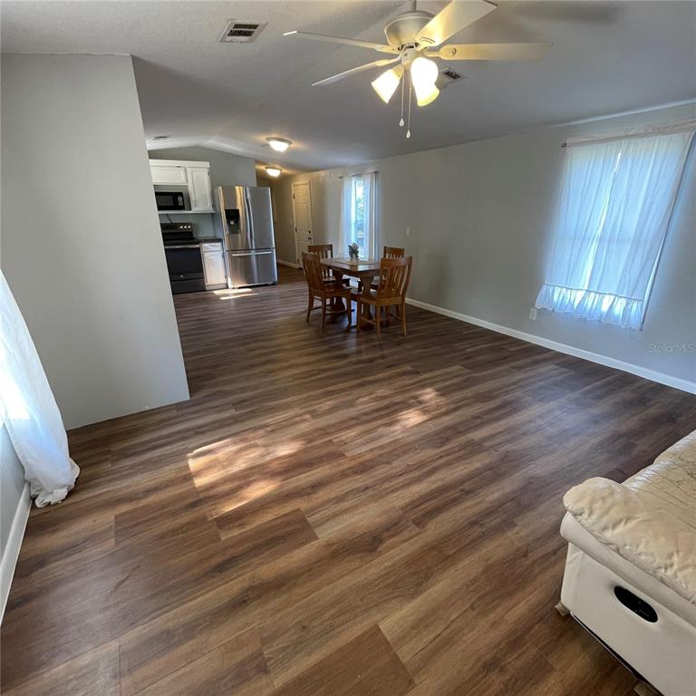 An open-concept living and dining area features wood-look flooring and a ceiling fan — 8771 NE 107TH COURT, BRONSON, FL