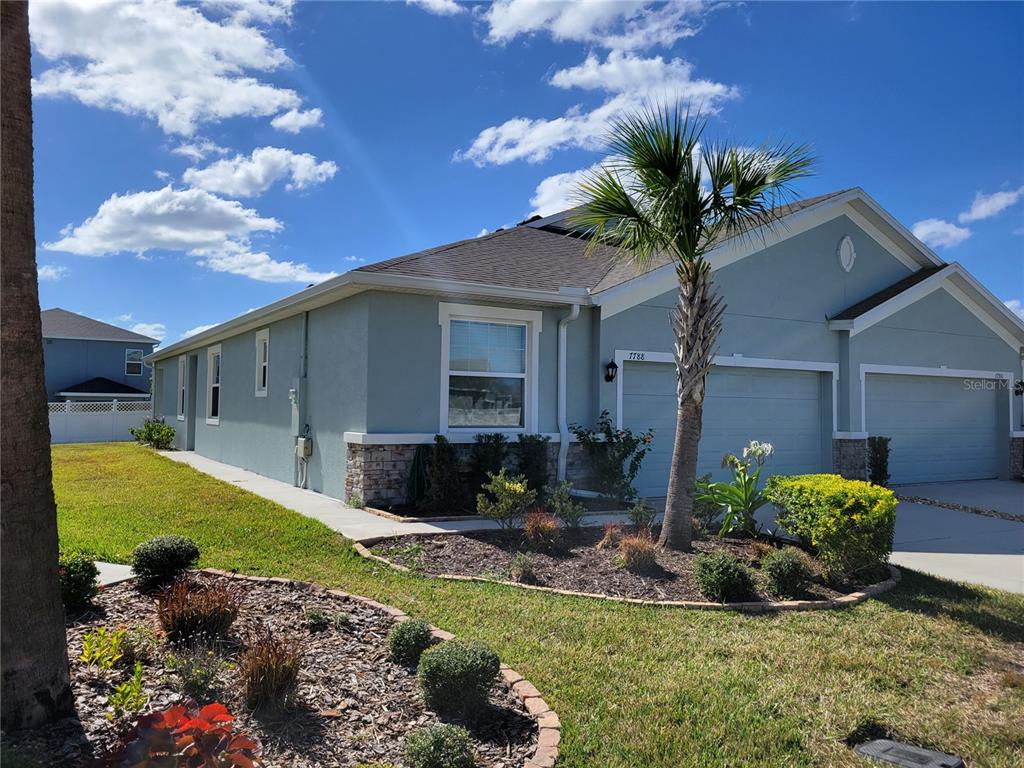 A light blue single-story house with a two-car garage and a palm tree in front — 7788 STONEBROOK CIRCLE, WESLEY CHAPEL, FL