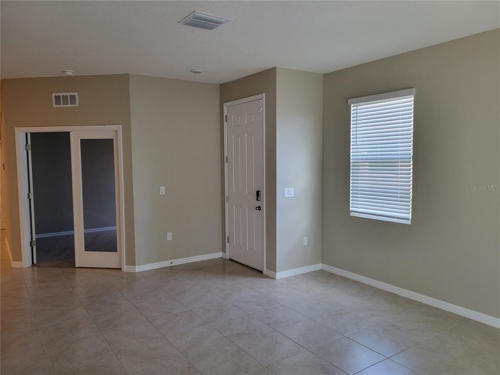 A room with light-colored tile flooring, beige walls, a window with blinds, and two doors — 7788 STONEBROOK CIRCLE, WESLEY CHAPEL, FL