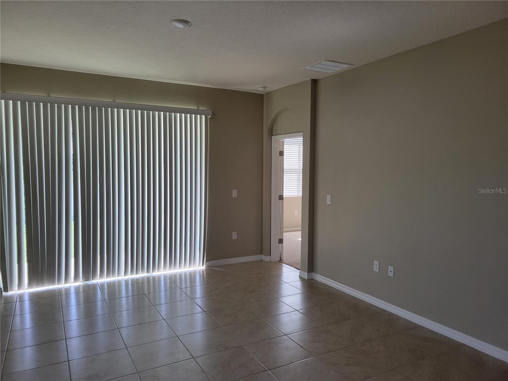 A room with tile flooring, beige walls, vertical blinds, and a doorway leading elsewhere — 7788 STONEBROOK CIRCLE, WESLEY CHAPEL, FL