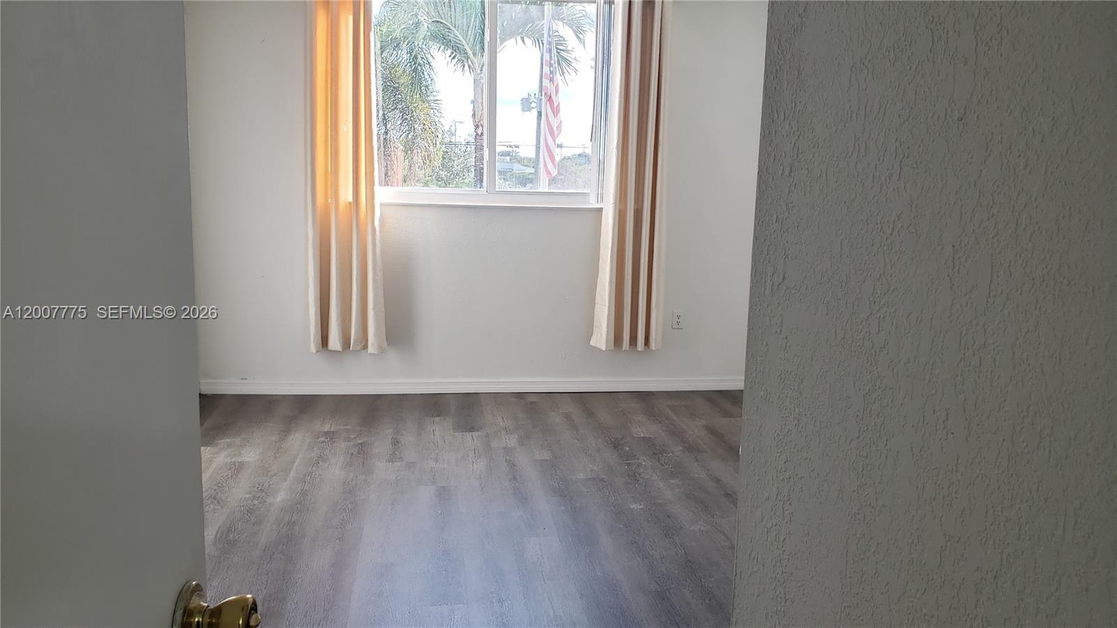 A bedroom features gray wood-look flooring, white walls, and a window with beige curtains — 1251 NE 108th St # 215, Miami FL 33161, MIAMI, FL
