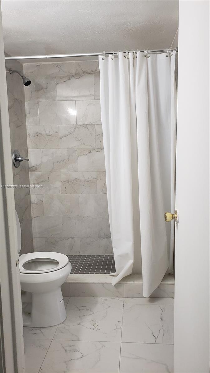 A bathroom features a tiled shower with a white curtain and a white toilet — 1251 NE 108th St # 215, Miami FL 33161, MIAMI, FL