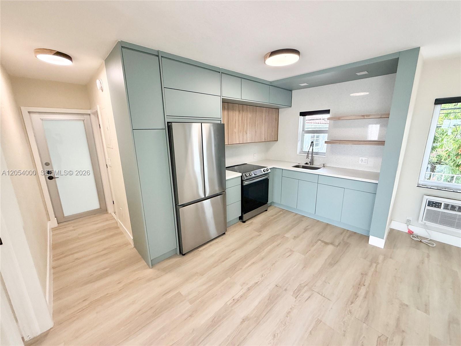 A modern kitchen features light blue cabinetry, stainless steel appliances, and light wood flooring — 641 Espanola Way # 17, Miami Beach FL 33139, MIAMI BEACH, FL