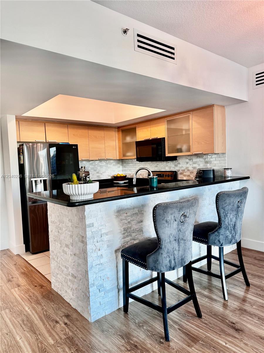 A kitchen features light wood cabinets, black countertops, a stone-tiled breakfast bar, and two chairs — 140 S Dixie Hwy # 921, Hollywood FL 33020, HOLLYWOOD, FL
