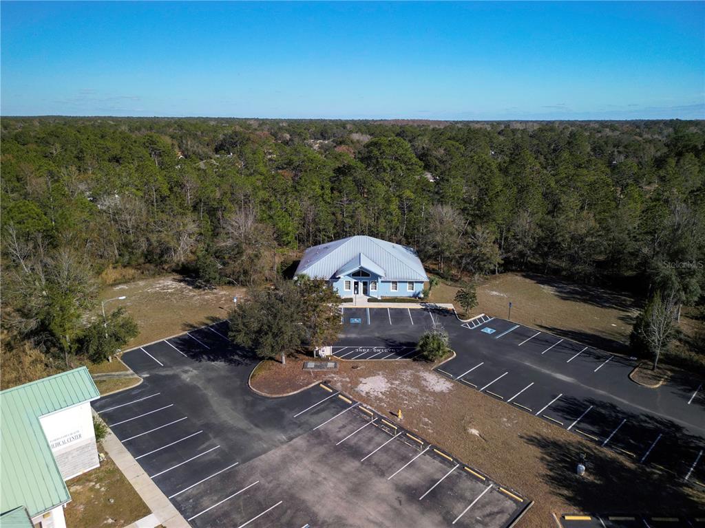 An aerial view shows a blue commercial building surrounded by a parking lot and forest — 8427 S SUNCOAST BOULEVARD, HOMOSASSA, FL