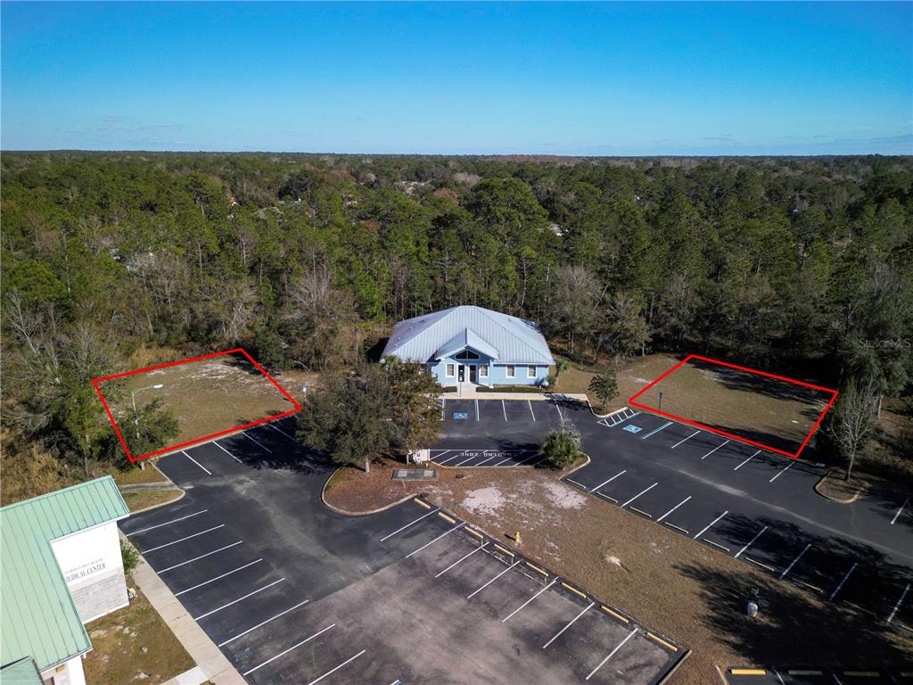 An aerial view shows a commercial building with two vacant, outlined lots in its parking area — 8427 S SUNCOAST BOULEVARD, HOMOSASSA, FL