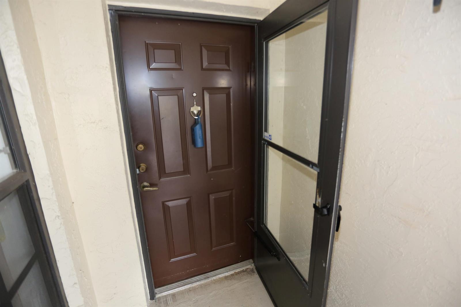 A brown front door with a glass storm door is set in a beige wall — 3277 Jog Park Drive, FL 33467, FL