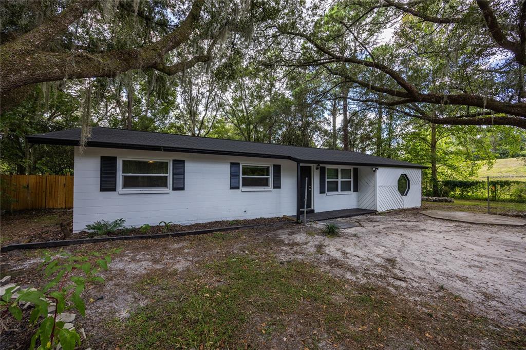 A single-story white house with black shutters and a dark roof sits among large trees — 14637 NE 145TH AVENUE, WALDO, FL
