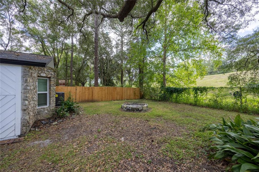 A backyard featuring a stone fire pit, a wooden fence, and a stone-sided building — 14637 NE 145TH AVENUE, WALDO, FL