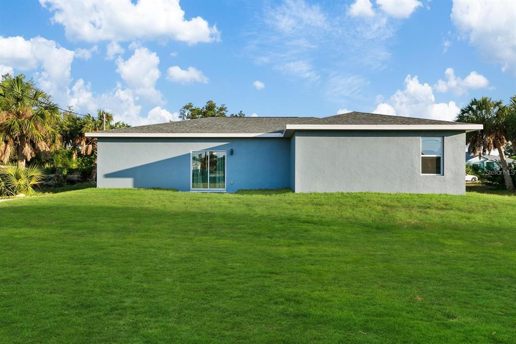 The rear exterior of a single-story house with gray stucco walls and a sliding door — 3038 SARGEANT STREET, PORT CHARLOTTE, FL