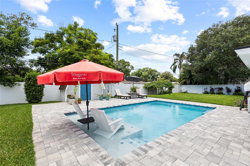 A backyard features a rectangular swimming pool with a tanning ledge and a red umbrella — 1821 OAK LAKE DRIVE, CLEARWATER, FL