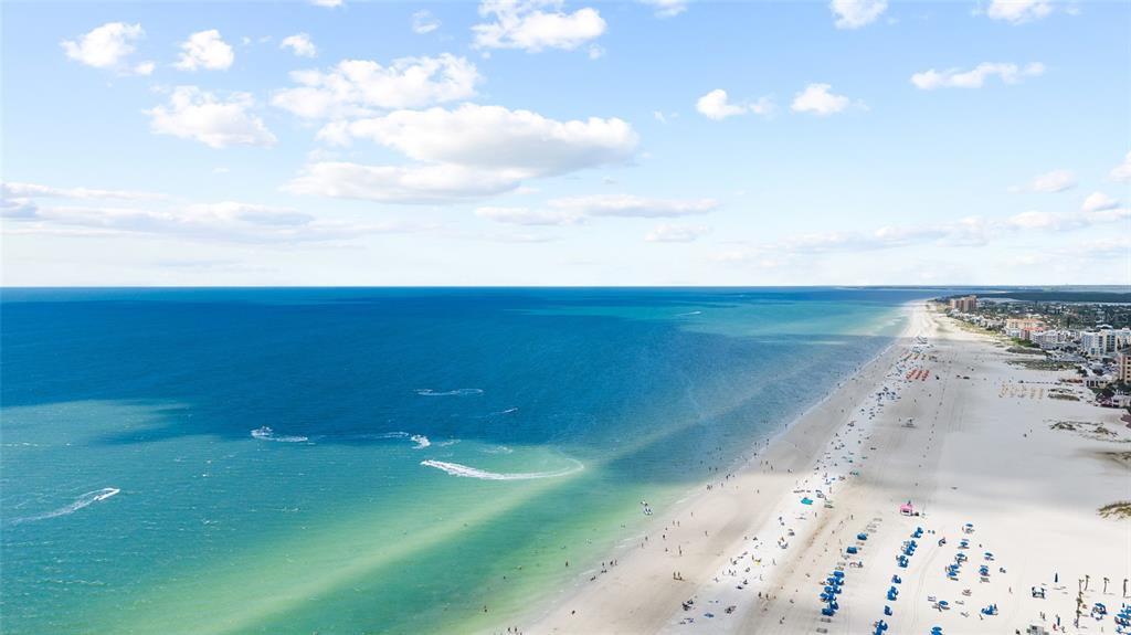 An aerial view of a wide, sandy beach along a blue ocean under a cloudy sky — 1821 OAK LAKE DRIVE, CLEARWATER, FL
