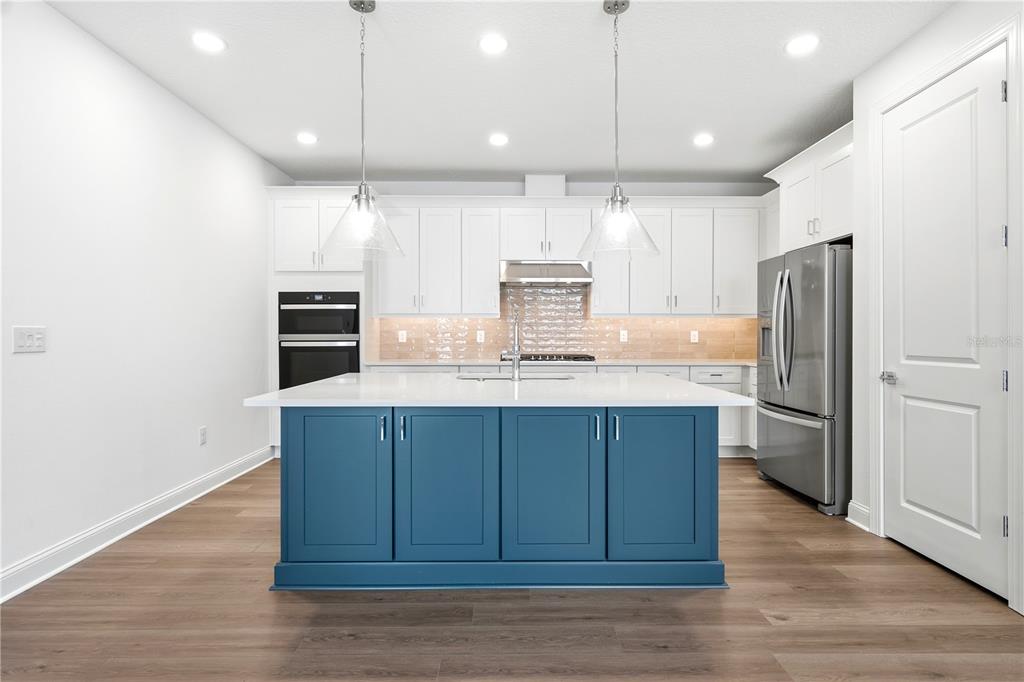 A modern kitchen features white cabinetry, a blue center island, and stainless steel appliances — 5854 WINDBREAK COURT, APOLLO BEACH, FL